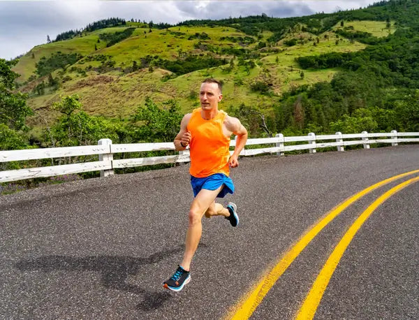 Guy running on the road with Topo Athletic running shoes in blue shorts and orange running tank top