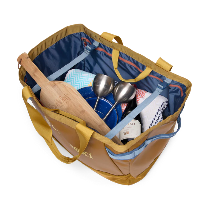 Open tote bag with kitchen items including a wooden spoon, wine bottle, and utensils on a white background