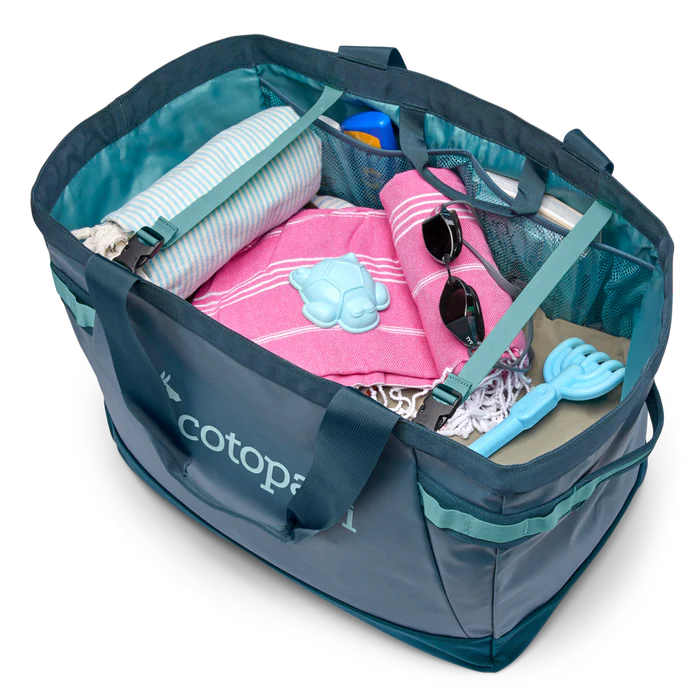 Blue and teal tote bag filled with beach items on a white background