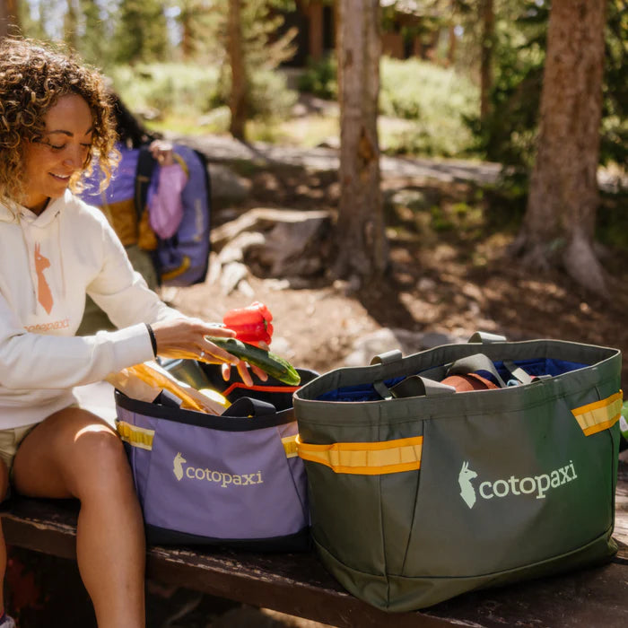 Person sitting outdoors with Cotopaxi bags in a forest setting
