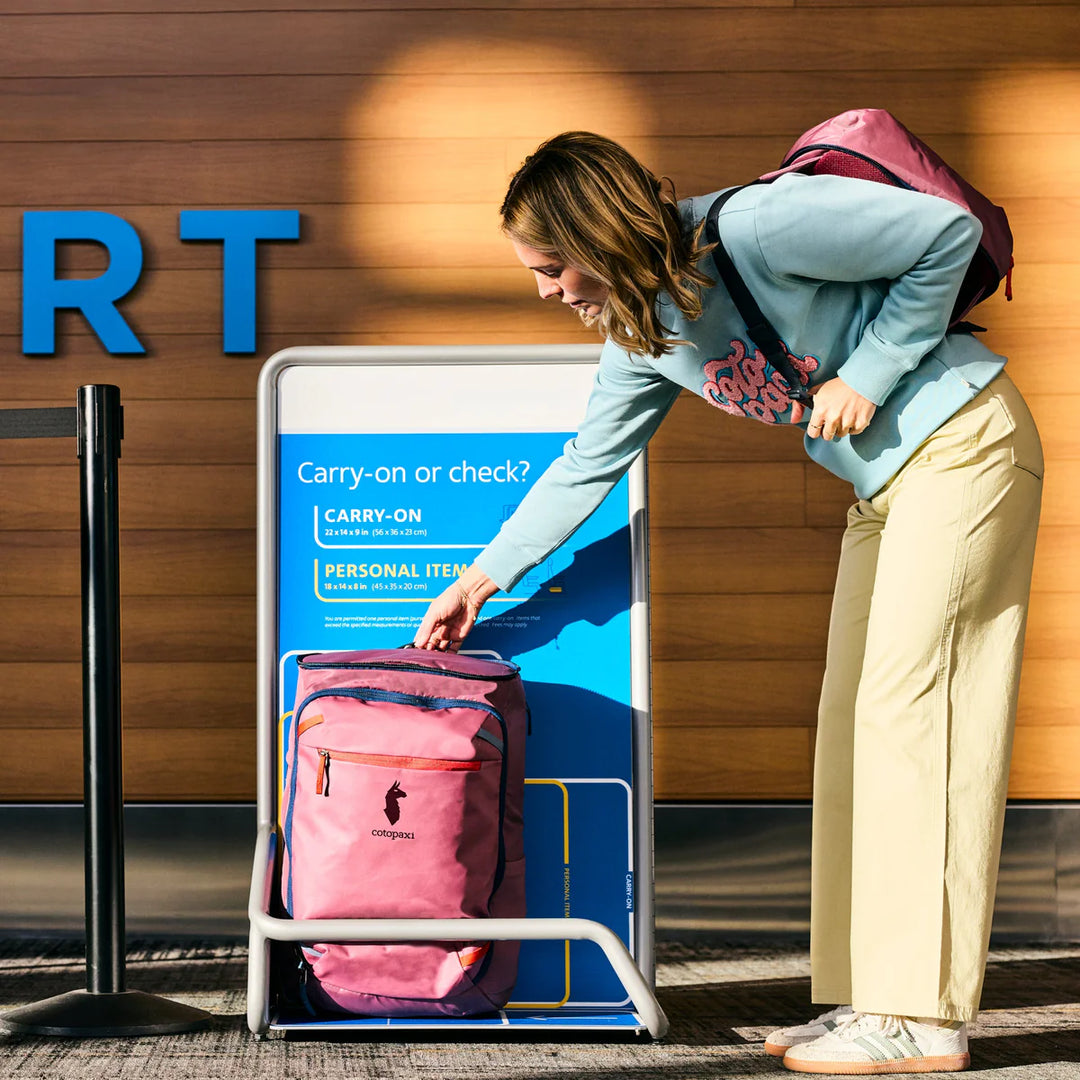Woman with a pink backpack interacting with a sign at an airport.