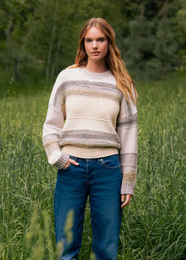 Woman wearing a striped sweater and blue jeans standing in a grassy field