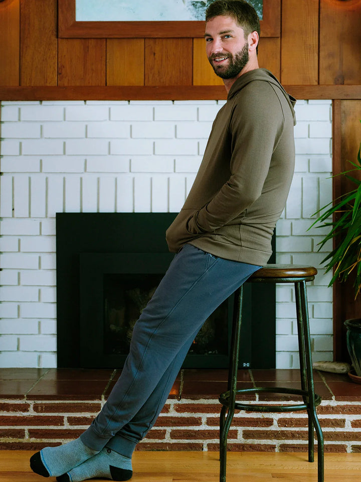 Man sitting on a stool in a room with a fireplace and white brick wall.