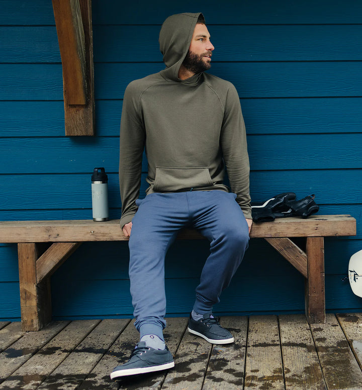 Man sitting on a wooden bench against a blue wall with outdoor gear nearby.