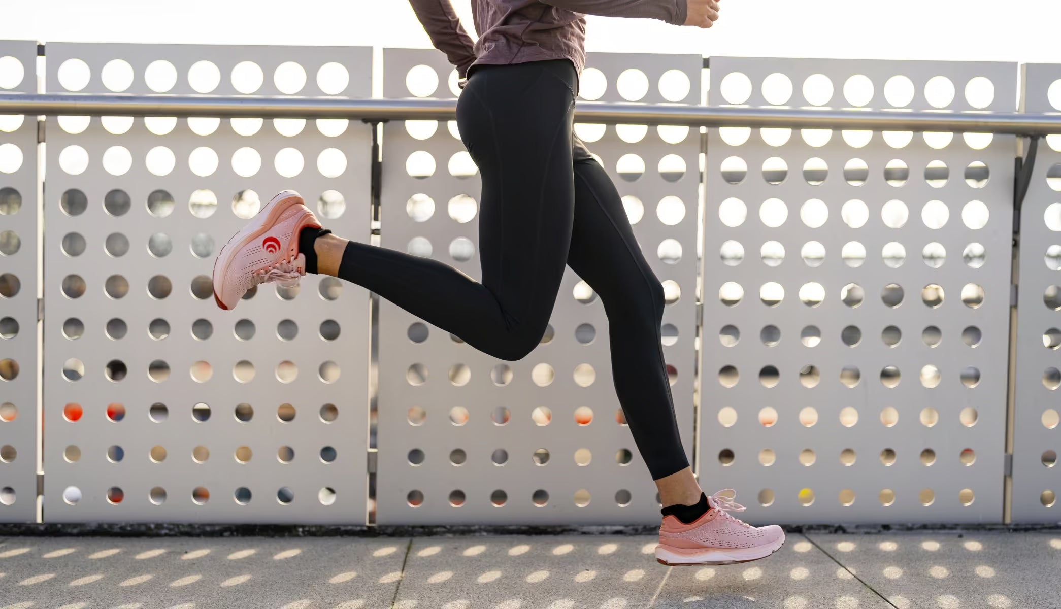 Person running on a bridge with a perforated metal fence in the background